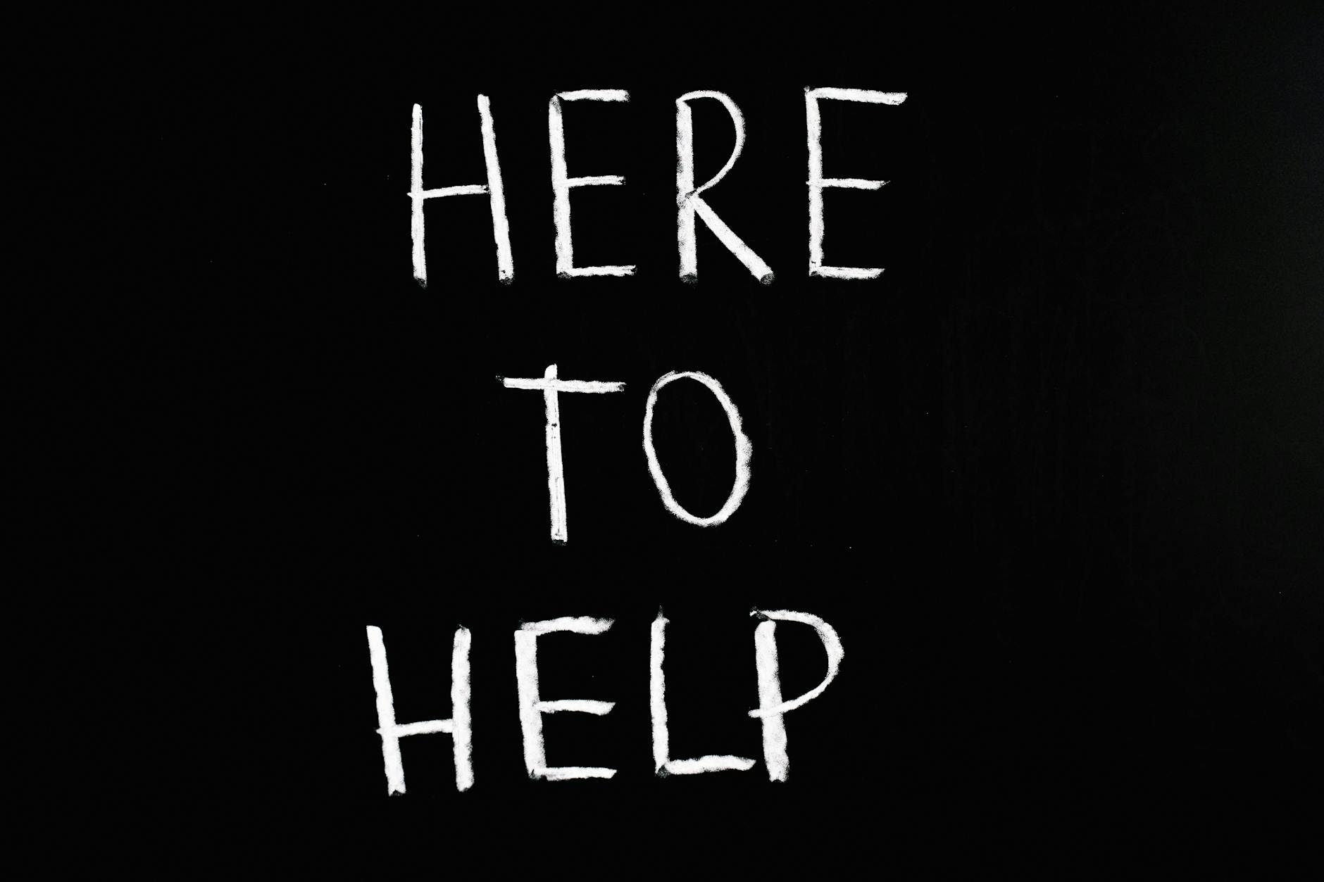 A chalkboard with the words 'HERE TO HELP' written in white letters on a black background.