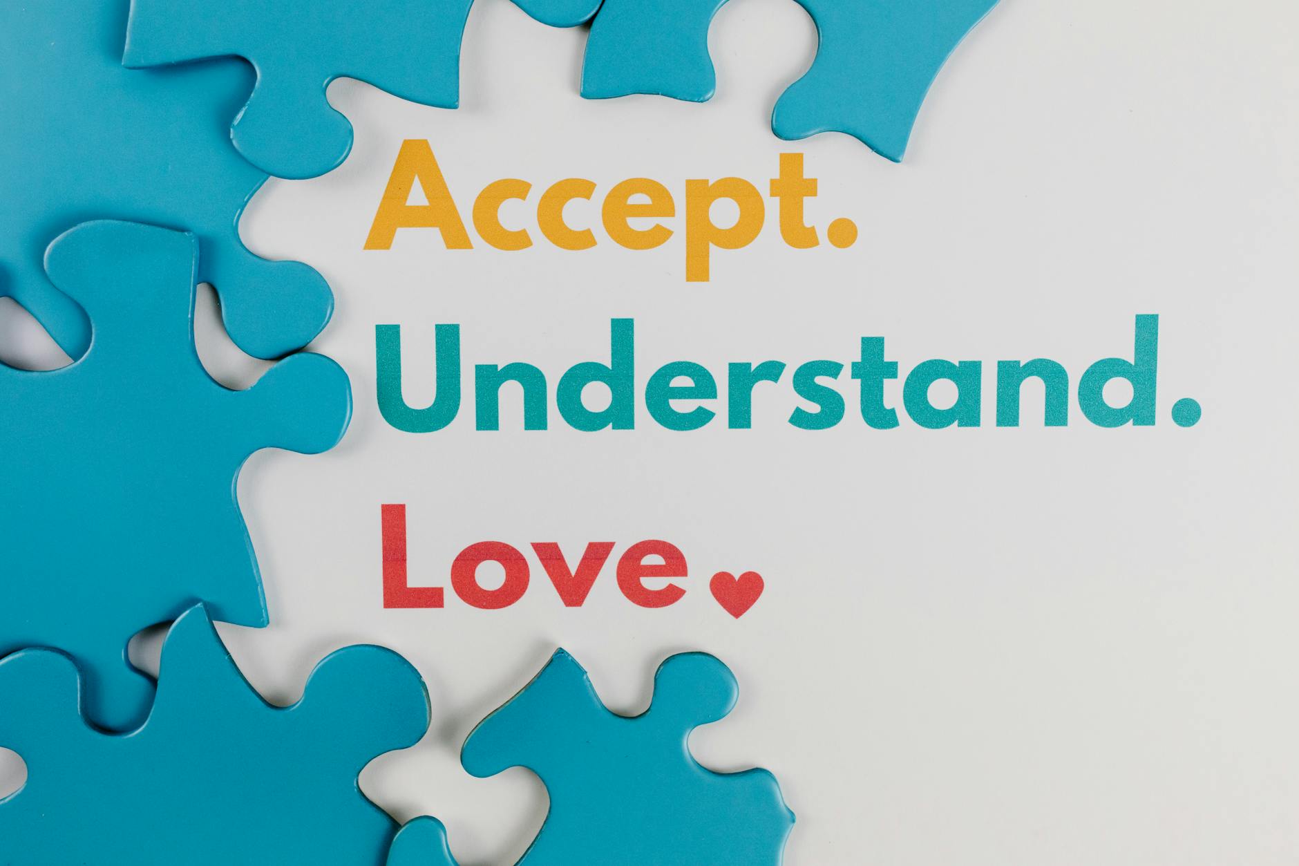 A close-up view of colorful puzzle pieces surrounding the words 'Accept. Understand. Love.' on a white background.