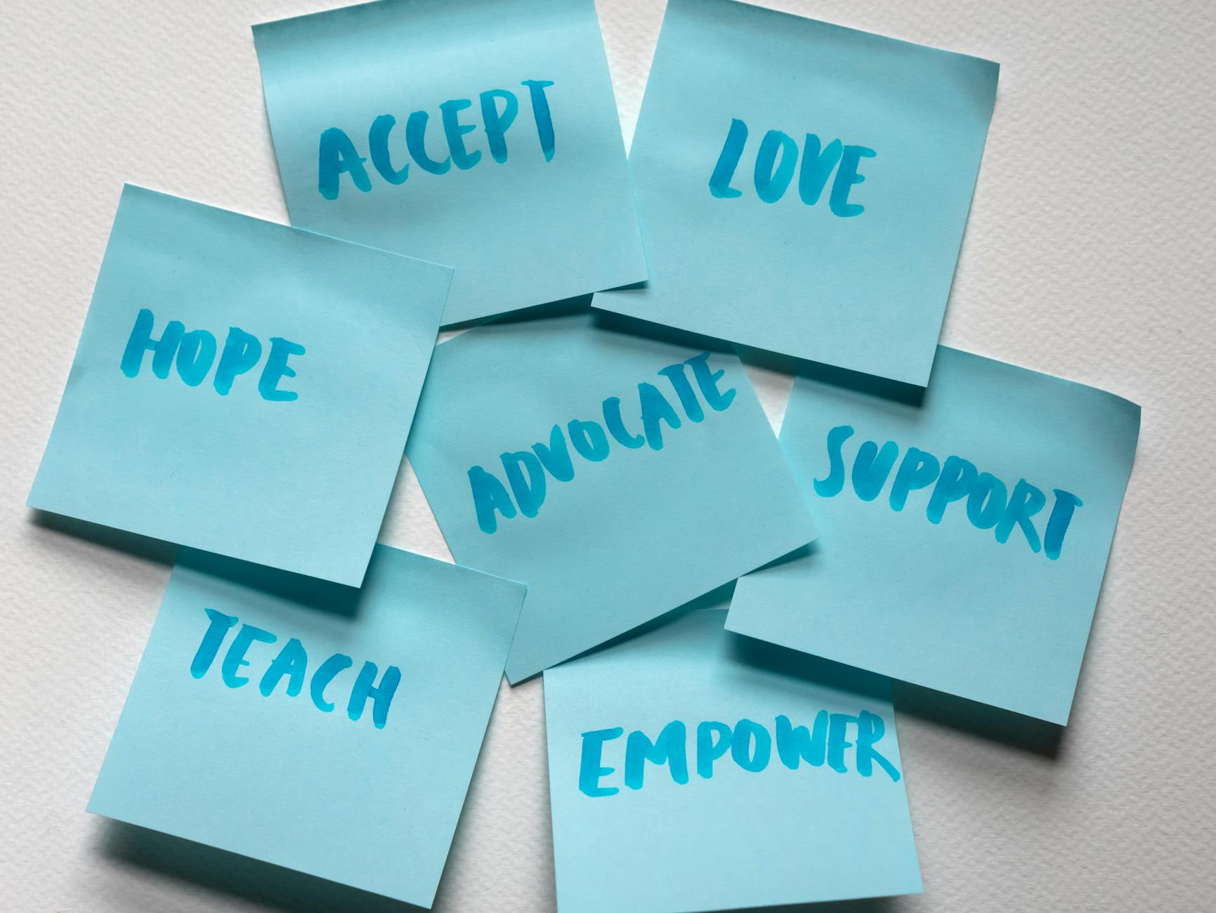 A collection of blue sticky notes with handwritten motivational words: 'ACCEPT', 'LOVE', 'SUPPORT', 'ADVOCATE', 'EMPOWER', 'TEACH', 'HOPE'.