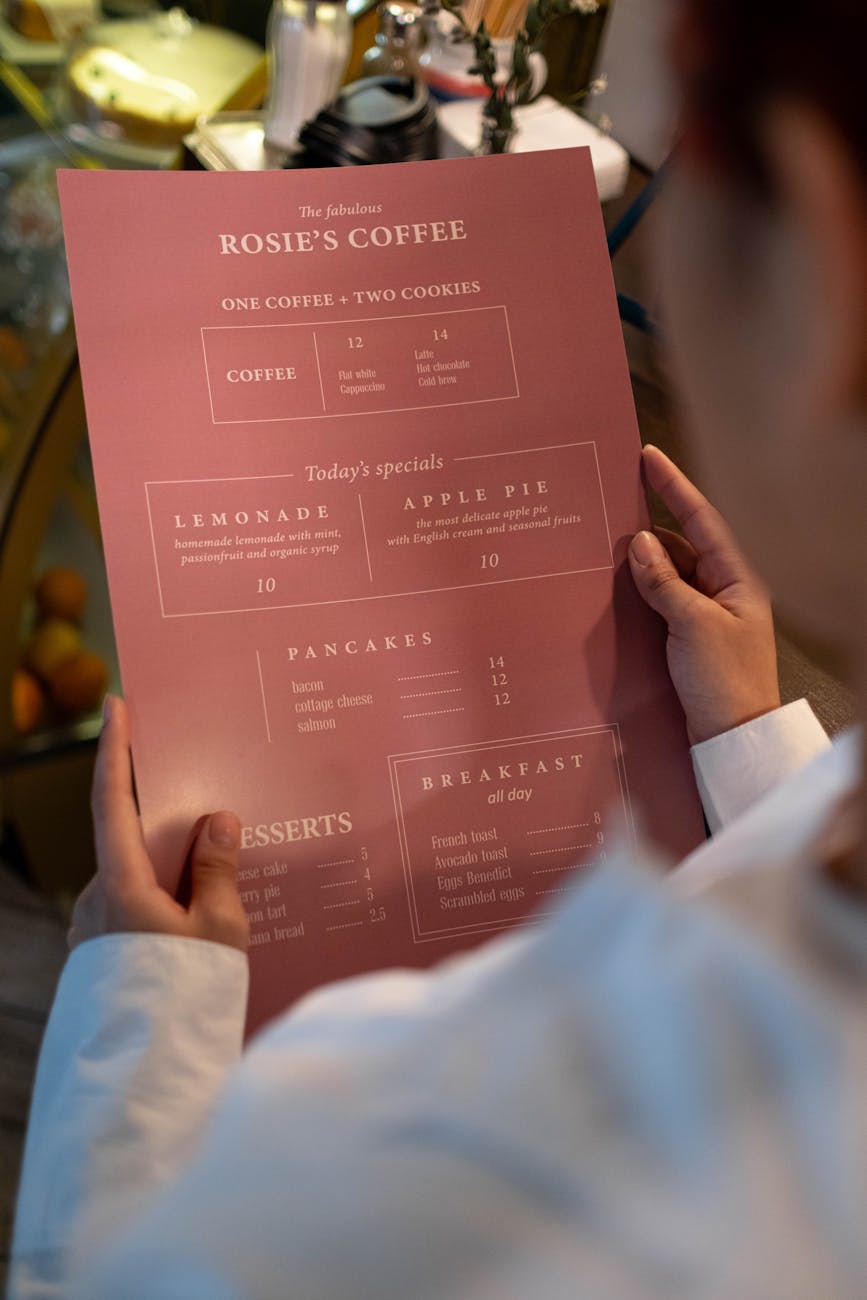 A person holding a pink menu titled 'Rosie's Coffee' displaying various food and beverage options in a cafe setting.