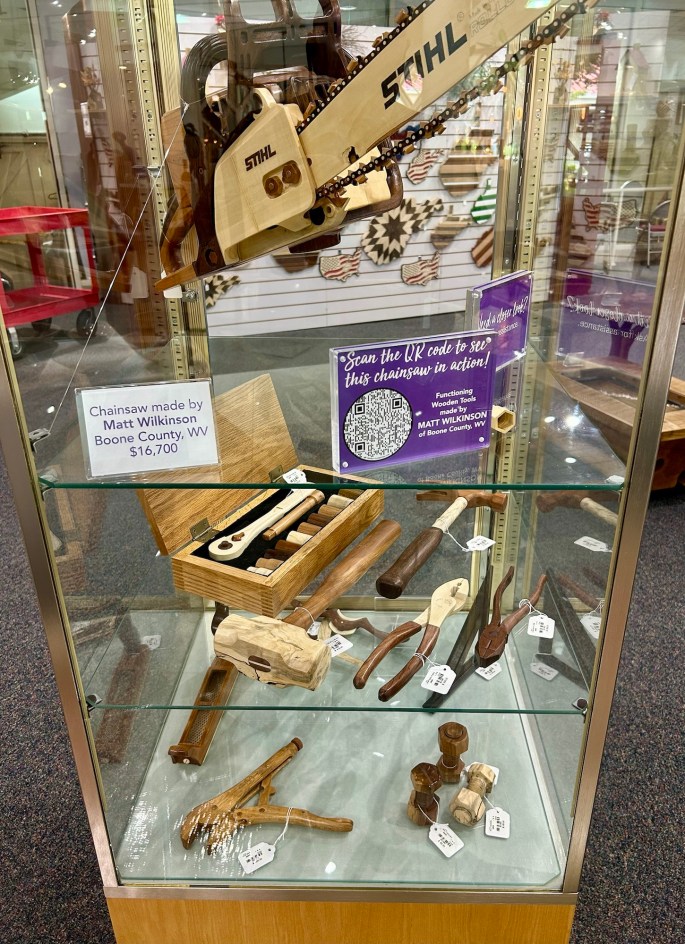 Showcase of handcrafted wooden tools and a chainsaw sculpture made by Matt Wilkinson from Boone County, WV, displayed in a glass case.