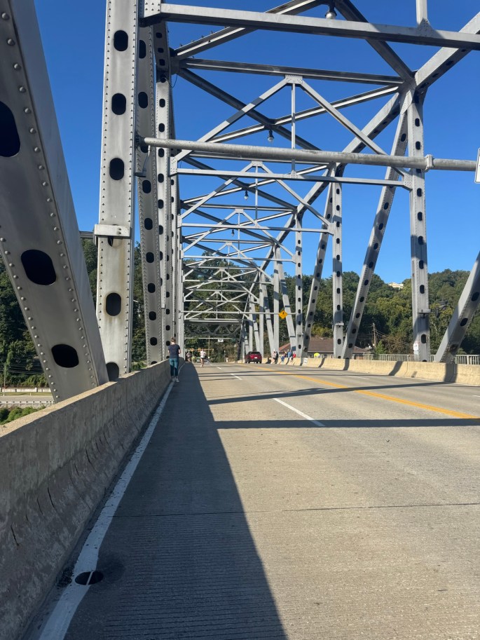 View of a bridge with steel beams and a roadway, featuring a few pedestrians in the distance.