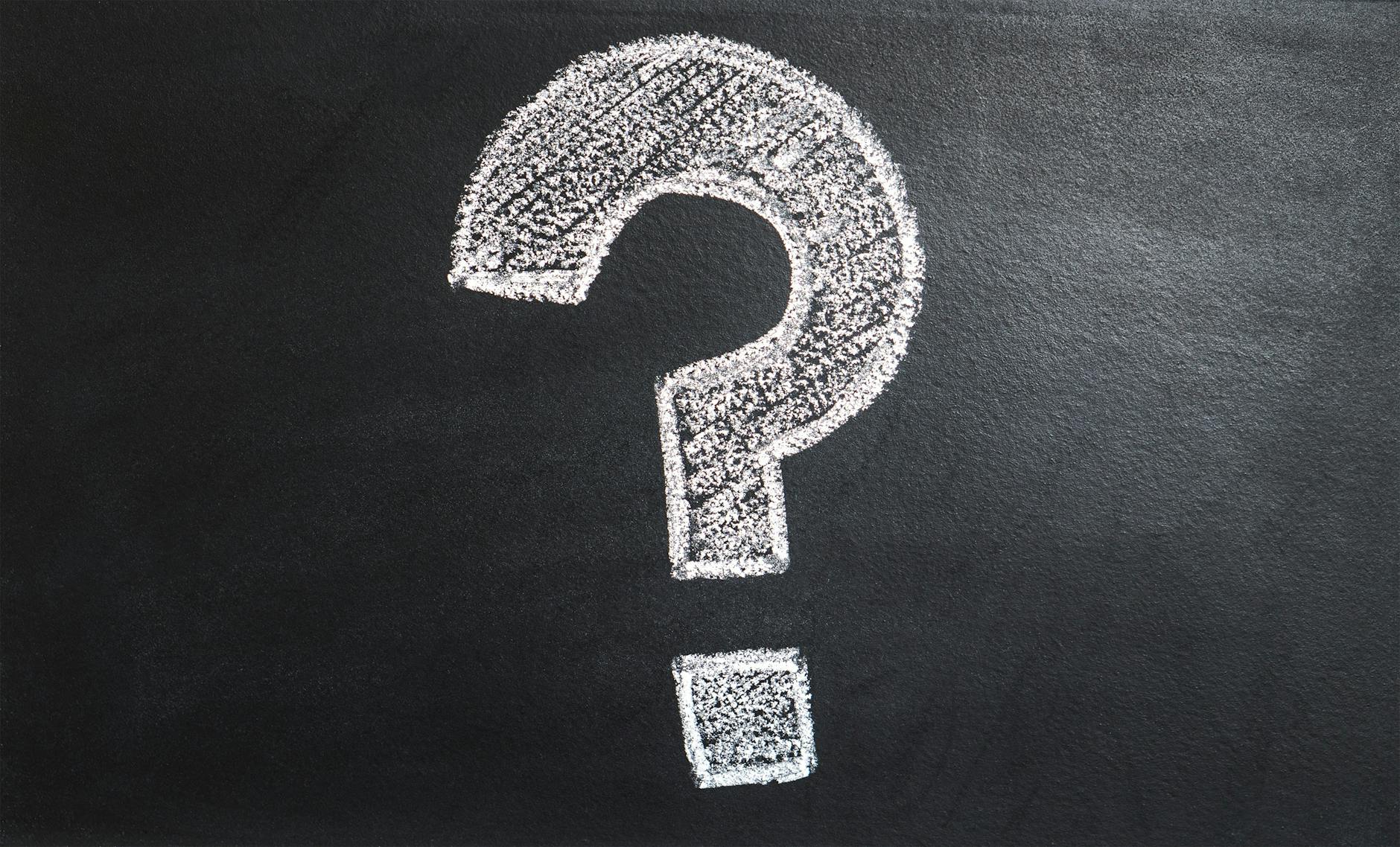 A chalk-drawn question mark on a black background, symbolizing uncertainty and curiosity.