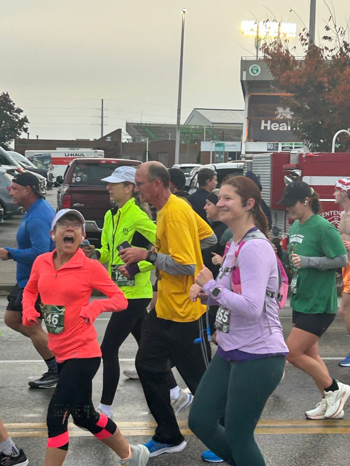 A group of runners participating in a marathon on an overcast morning, with diverse individuals wearing colorful athletic clothing and cheerful expressions.