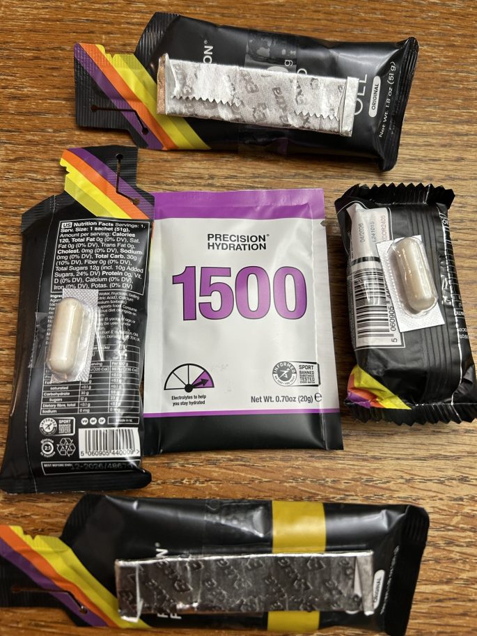 An assortment of hydration and energy products for runners, including electrolyte tablets and energy gels, arranged on a wooden surface.
