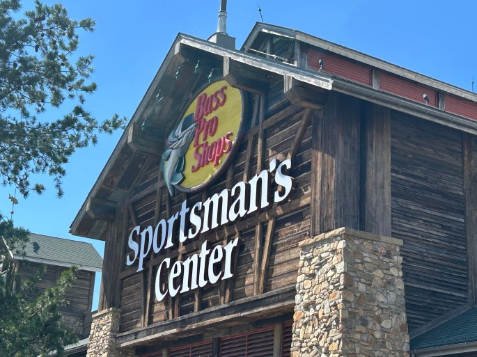 Exterior view of the Sportsman's Center building under a clear blue sky, featuring a wooden structure with a prominent sign for Bass Pro Shops.
